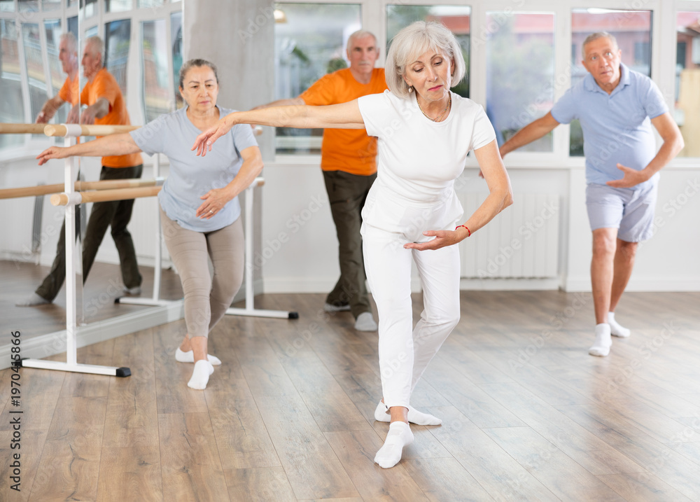 Obraz premium Happy aged woman in sportswear confidently leading ballet class with dancers following movements in modern dance studio