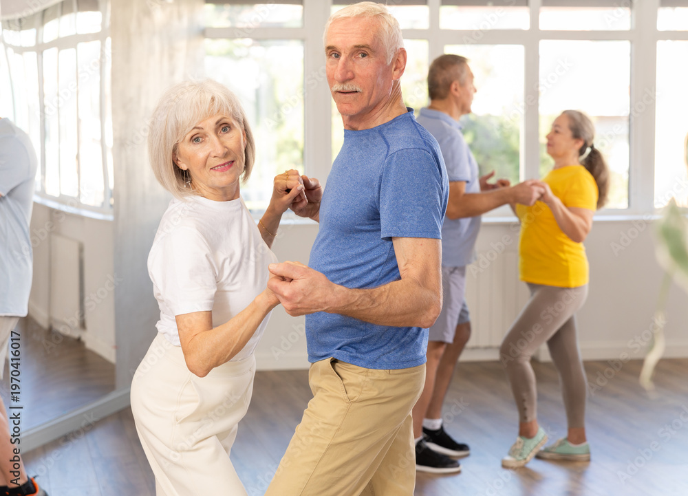 Fototapeta premium Group of happy elderly pensioners learning to dance latin dances in dance studio