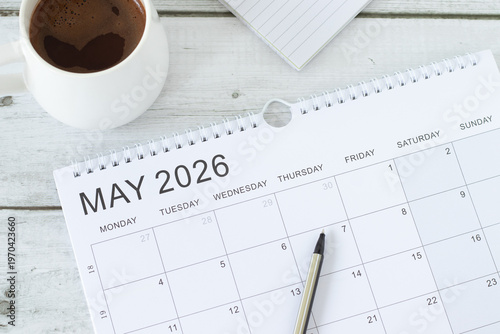 May 2026 calendar month with cup of coffee and notebook on wooden background. Top view.