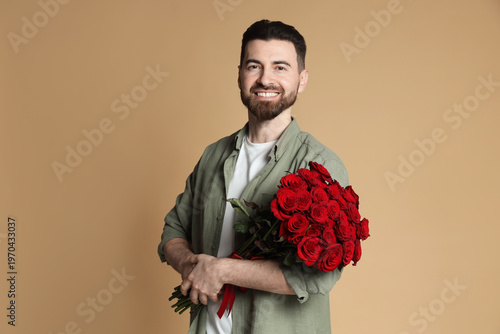 Handsome man with bouquet of roses on beige background