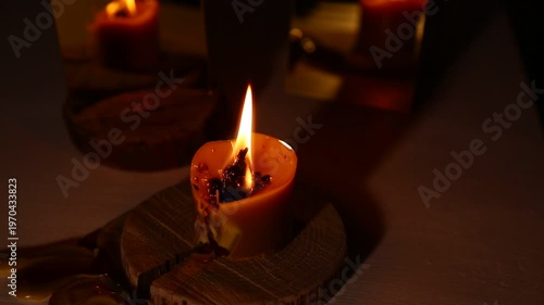 A brightly burning candle against a dark background near a mirror, the candle flame dripping melted wax onto the table. A magical witch ritual.