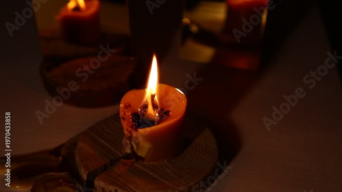 A brightly wind burning candle against a dark background near a mirror, the candle flame dripping melted wax onto the table. A magical witch ritual.