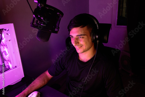 Quadro em tela Young caucasian male streamer smiling and looking at computer screen with neon p