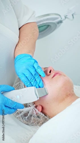 A professional esthetician cosmetologist performs ultrasonic facial cleansing peeling, deeply exfoliating the skin and cleaning pores.