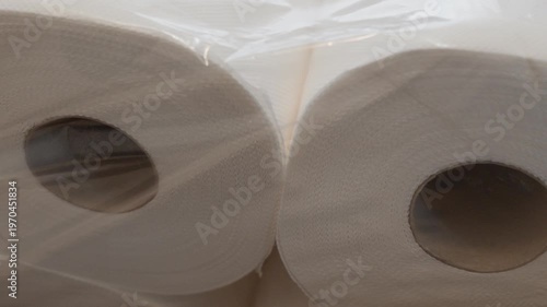 Close-up of two toilet paper rolls wrapped in plastic. Focus on compressed layers and packaging detail in soft lighting.