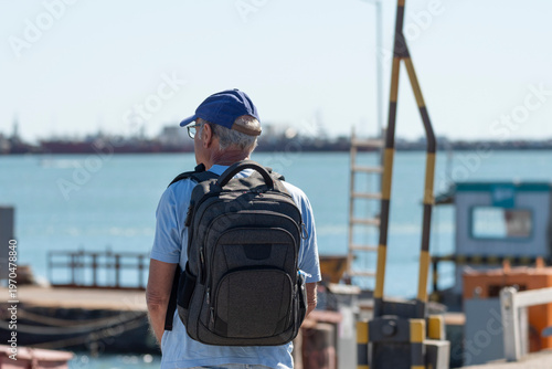 Medio cuerpo hombre mayor de espalda con mochila contemplando  paisaje  marino con desenfoque