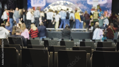 Empty audience seats in venue with blurred bustling crowd on stage
