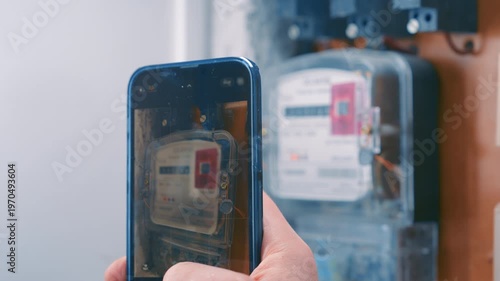 Close-up of Hand Holding Smartphone and Taking Picture of Electric Meter Readings | Smart Meter Monitoring and Utilities | Monthly Power Consumption Check in Residential Apartment