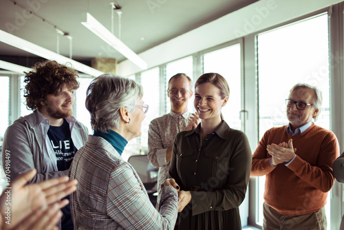 Colleagues applauding promotion handshake in modern office