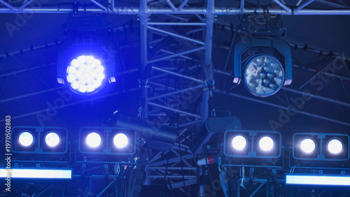 Concert stage lighting equipment shining blue spotlights on truss structure