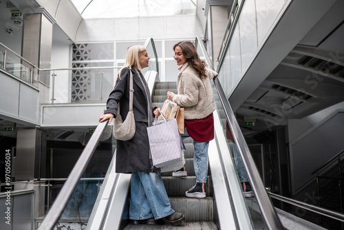 Konstfotografi Women friends talking on escalator with shopping bags