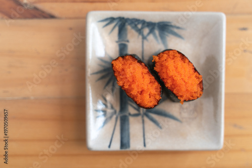 Close-up of two pieces of tobiko sushi (flying fish roe) on a ceramic plate.