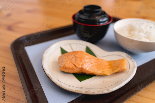 Japanese-style meal with grilled salmon, a bowl of rice, and an empty soup bowl on a tray.