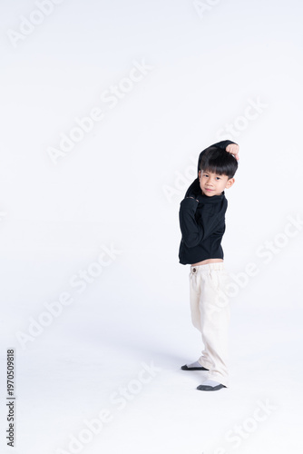 Young boy stretching his arm, standing against a plain white background.