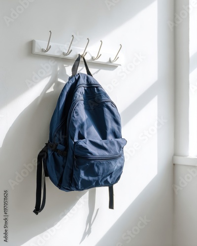 A navy blue backpack with clean lines, hanging on a white wall hook