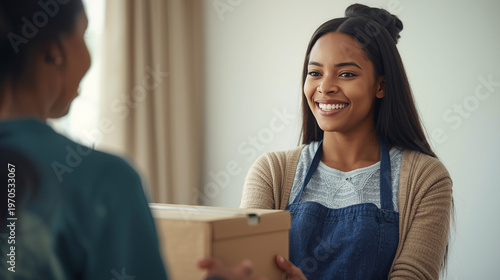 Happy young shop assistant in an apron handing a package to a customer with a warm welcoming smile.