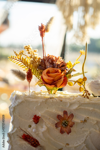 Rectangular white frosted cake elegantly decorated with dried autumn-toned flowers.
