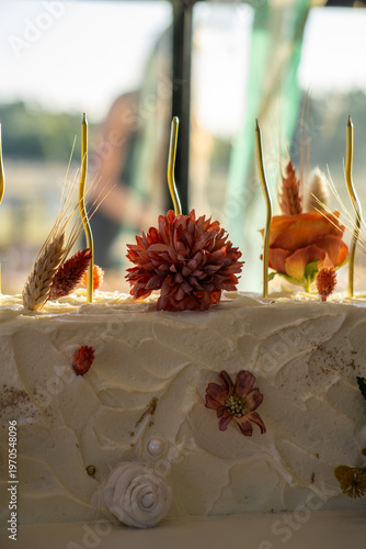 Rectangular white frosted cake elegantly decorated with dried autumn-toned flowers.