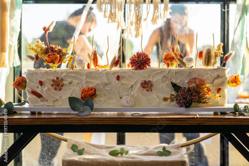 Rectangular white frosted cake elegantly decorated with dried autumn-toned flowers.