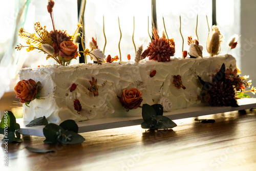 Rectangular white frosted cake elegantly decorated with dried autumn-toned flowers.