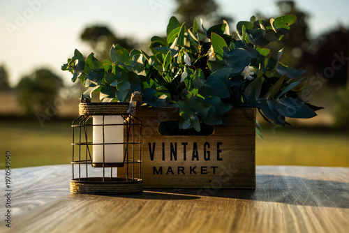 Vintage wooden crate with green foliage next to a rustic lantern on a wooden surface.
