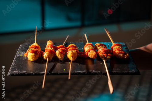Crispy fried skewers topped with red sauce served on a slate platter.