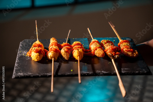 Crispy fried skewers topped with red sauce served on a slate platter.