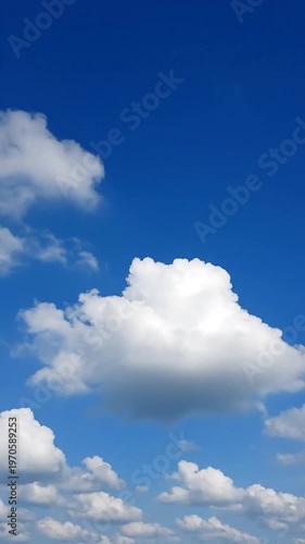 Fluffy white clouds drift across a vast, clear blue sky on a bright, sunny day