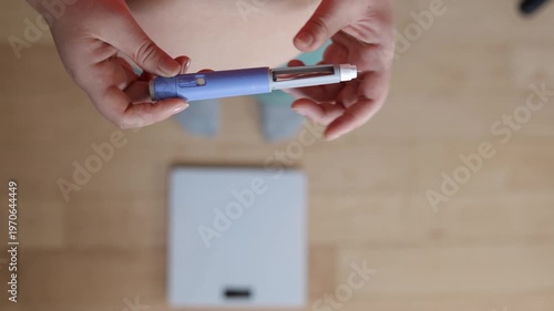 A horizontal close up shot. A young woman primes the pen injector, preperes it for injection
A young woman primes pre-filled pen injector with semaglutide on floor and scales background