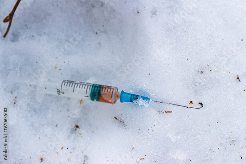 Gritty, discarded syringe with drug residue pollutes winter snow. A stark symbol of addiction, public health hazard, and environmental blight, found in a frozen landscape