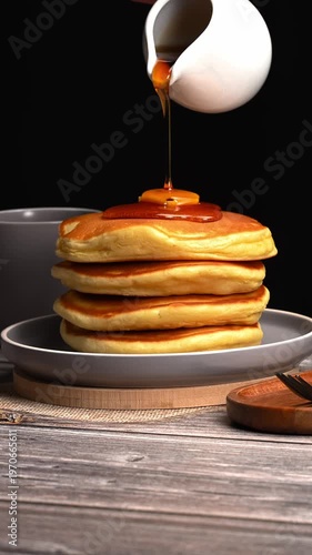 Close-up of golden pancakes with maple syrup being served from a white pitcher, classic hot cakes