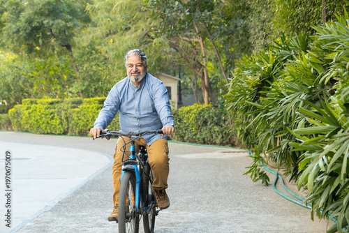 Retired Active fit senior indian asian man in 60s enjoy riding bicycle outdoor in summer. Retirement life. Healthcare and fitness. Vitality.