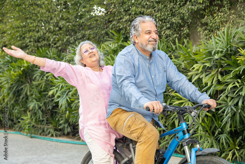Retired Active senior indian couple riding bicycle together, freedom and adventurous spirit in 60s. Healthy fit Elderly husband wife enjoy Retirement life. Fitness and vitality.