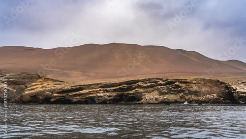 An ancient Inca Trident geoglyph on a hill. Drawing of the famous candelabra on a sandy slope. The rocky shore of the island. The ocean is in the foreground. Peru. Paracas.
 