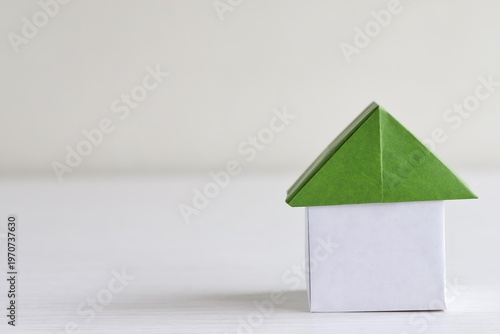 A close up shot of a house with green roof made of Japanese Origami paper on white wooden table. 