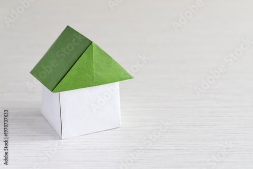 A close up shot of a house with green roof made of Japanese Origami paper on white wooden table. 