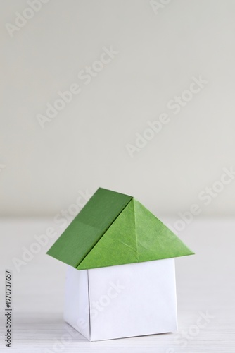 A close up shot of a house with green roof made of Japanese Origami paper on white wooden table. 