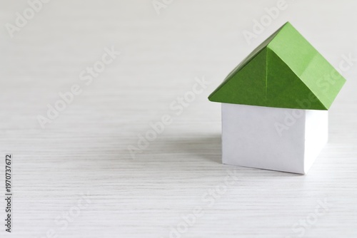 A close up shot of a house with green roof made of Japanese Origami paper on white wooden table. 