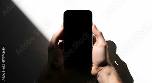A person holds a smartphone in their hands, casting a shadow on a white background.
