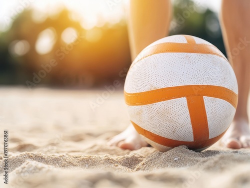 A volleyball on sandy beach near a player's feet during sunset, capturing a casual and active beach sports moment.