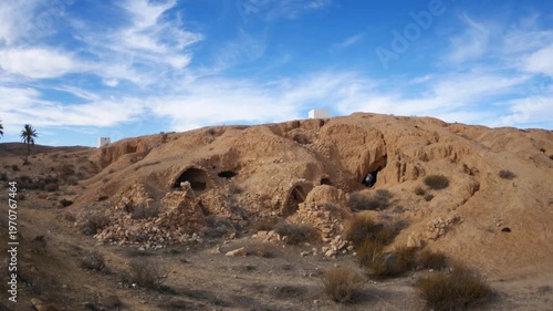Panorama: Traditional troglodyte houses carved into rock in Matmata, Tunisia. Ancient underground dwellings in arid desert landscape, historic Berber architecture and cultural heritage site