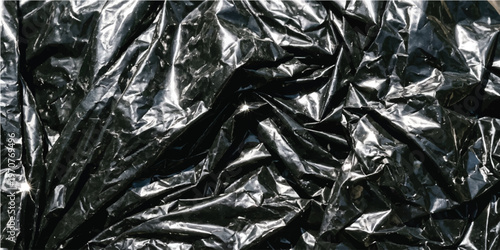 Close up view of crumpled black plastic sheet with deep folds and sharp highlights reflecting bright light on the dark glossy surface texture