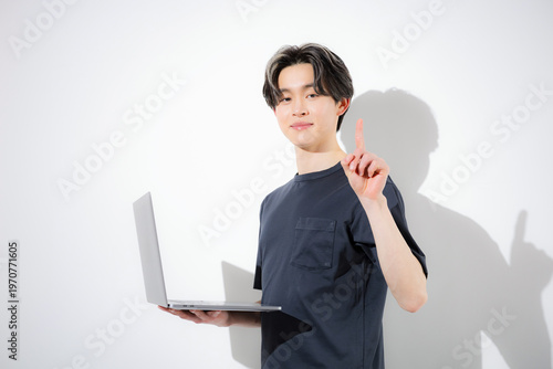 ノートパソコンで作業する若いフリーランスエンジニアやデザイナーなどの白背景カメラ目線　プログラミングで効率化や時短でaiを使うイメージの指差しでポイントやオススメのポーズ