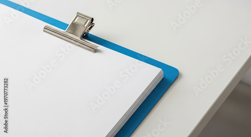 Blank clipboard on white desk with blue clip for organization  