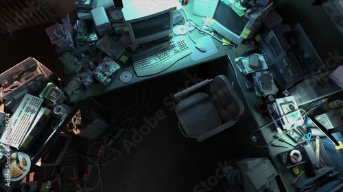 A cluttered old seedy office workstation at night, with retro 1990s period computer equipment and assorted electronics gear stripped down for repair - high rotating bird's eye view