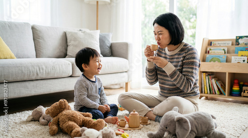 Asian Mother and Toddler Son Playing Tea Party on Rug in Modern Living Room, Family Bonding Moment