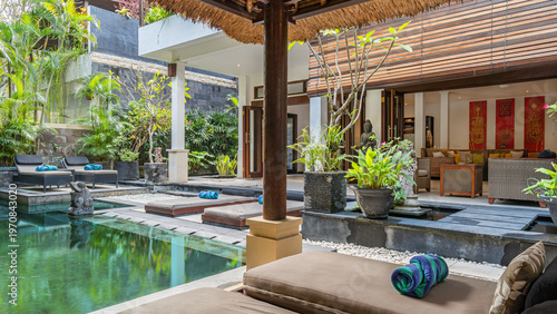 A pool with a wooden deck and a bamboo roof. The pool is surrounded by a lush green garden