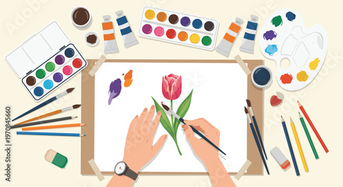 Overhead view of artist hands painting a red tulip flower with watercolors surrounded by various paints, brushes, and art supplies.