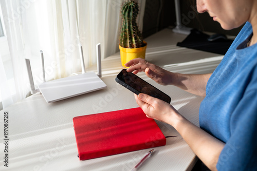 Cuadro en lienzo Woman Using Smartphone Near Wi-Fi 6 Router and Red Notebook on White Desk in Sun