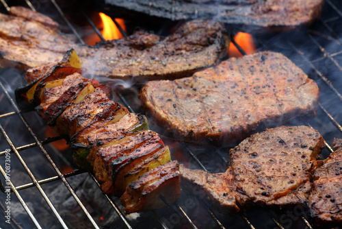 Overcooked meat skewers and partially burnt steaks on the grill, surrounded by smoke and fire, burnt meat is harmful to health and should not be eaten